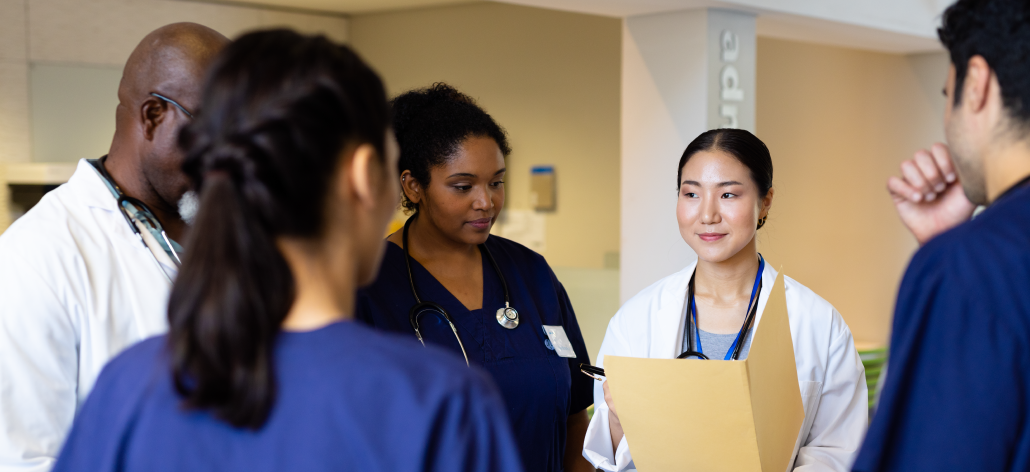 Group of healthcare professionals in scrubs and lab coats gathered in discussion.