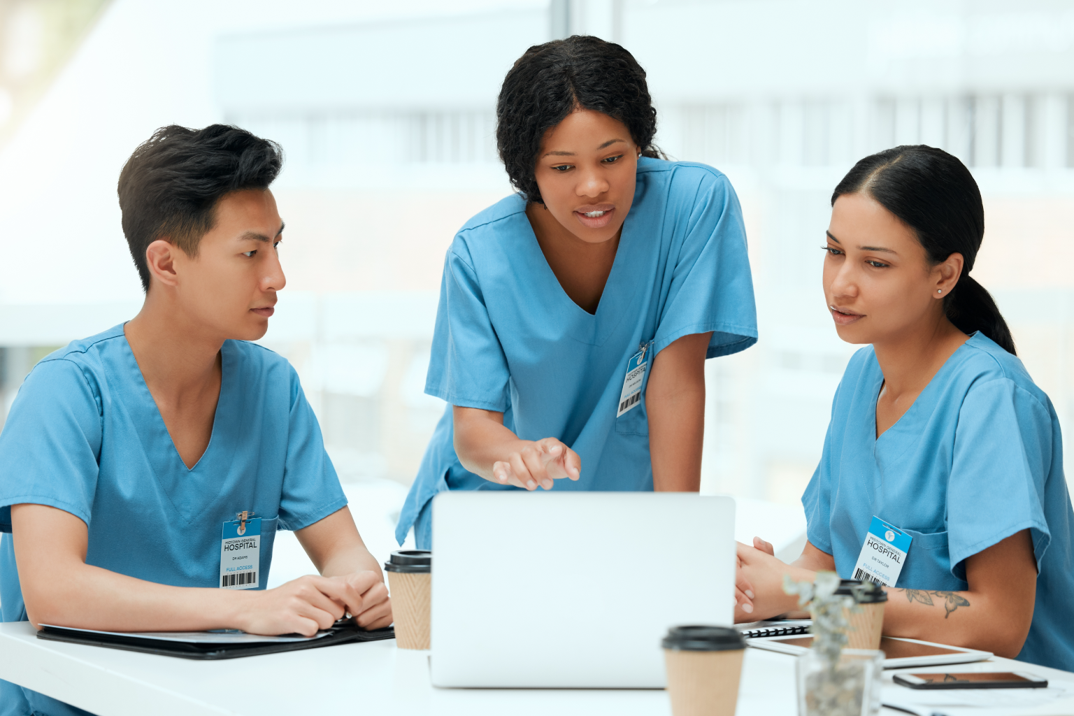 Three healthcare providers in blue scrubs work with a laptop