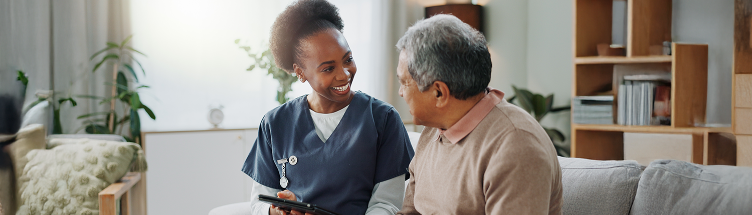 Smiling nurse and patient are in conversation on couch in an office setting.