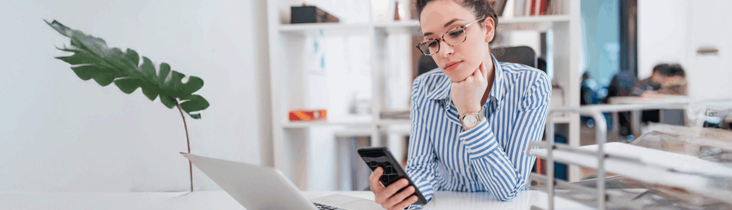 Woman in a striped blouse looks at her phone in the office.