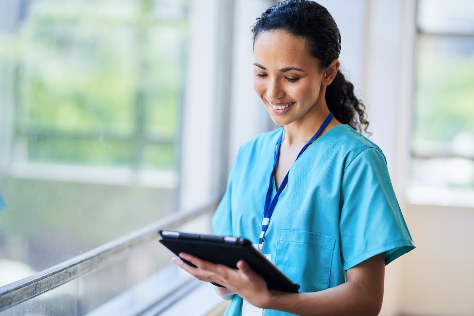 Nurse in scrubs smiling while looking at a tablet.