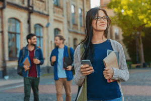 Woman wearing cardigan and blue shirt walks around campus on her phone.