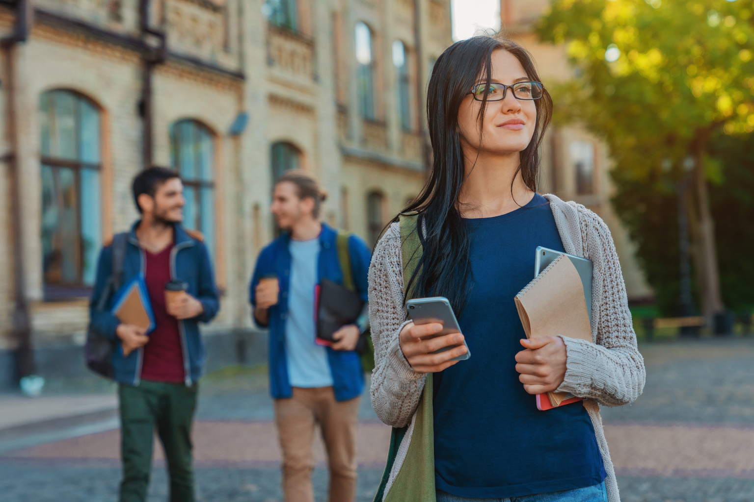 Woman wearing cardigan and blue shirt walks around campus on her phone.